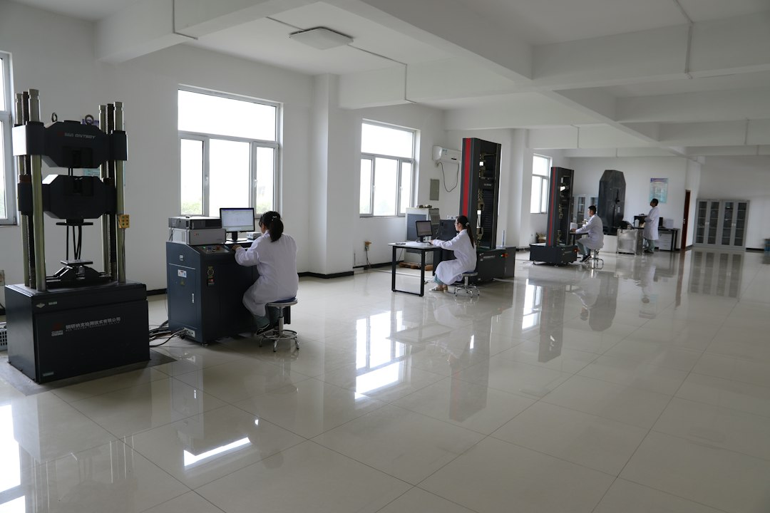A bright materials-testing laboratory where several people in white lab coats work at equipment stations